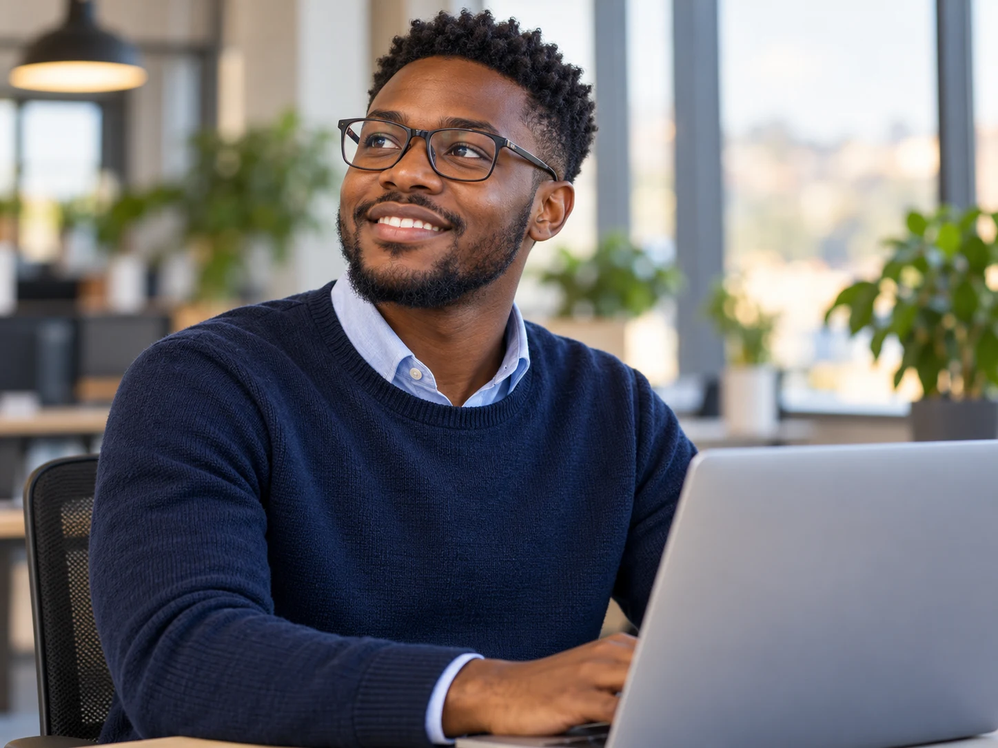 A smiling professional wearing glasses, seated at his laptop